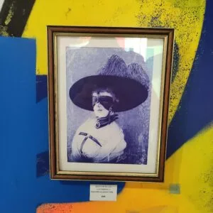 Tableau encadré d'une femme masquée à grand chapeau noir.