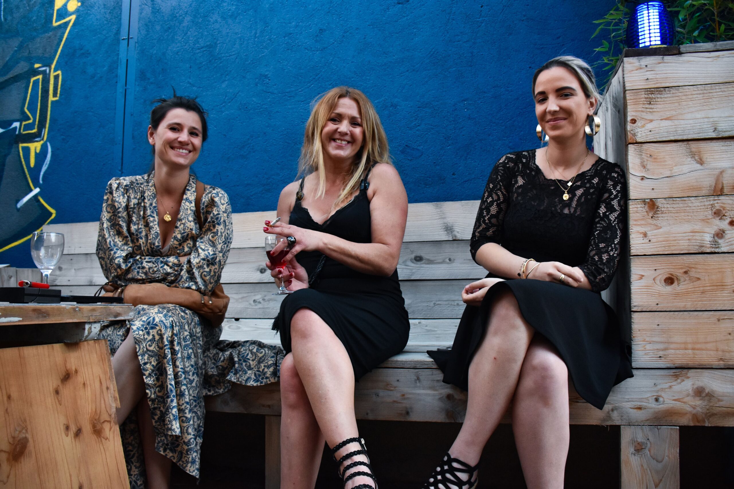 Trois femmes souriantes en soirée extérieure.