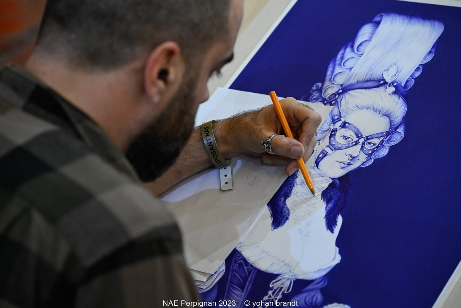 NAE2023-perpignan0228_yohanbrandt Artiste dessinant un portrait stylisé sur papier bleu.